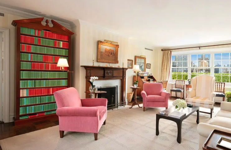 A fancy penthouse living room with fire place and a floor to cieling bookcase filled green and red books.